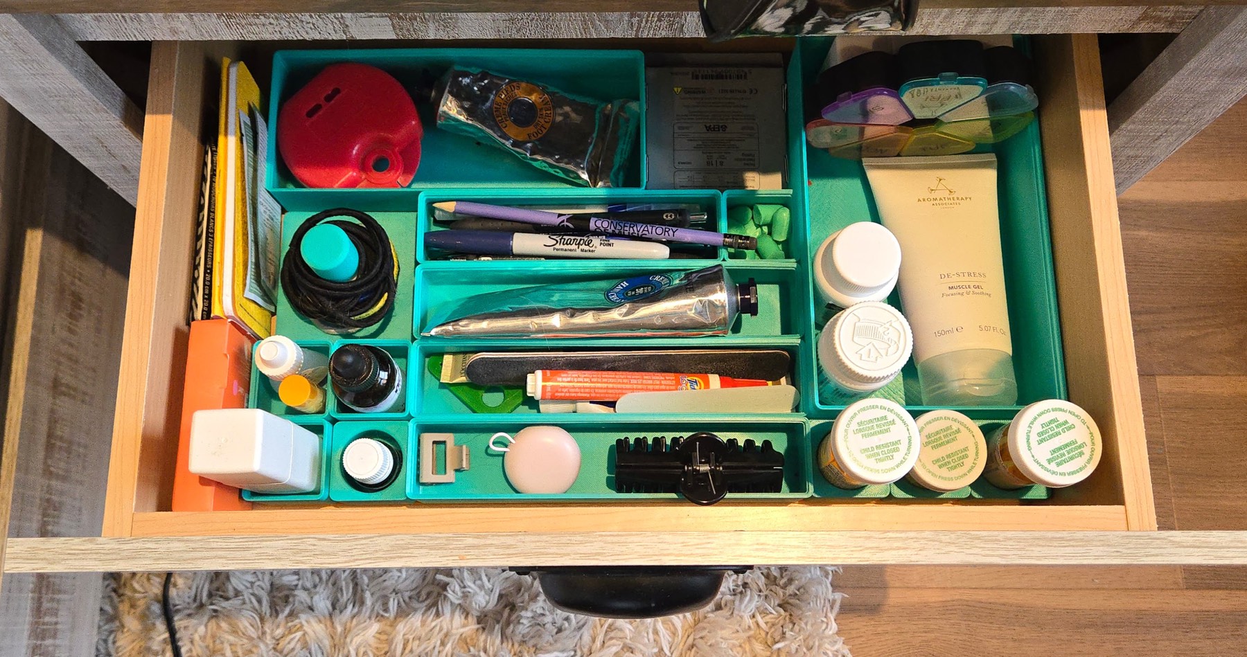 Overhead view of a drawer organized with modular teal bins separating grooming supplies, medication, and first-aid items.